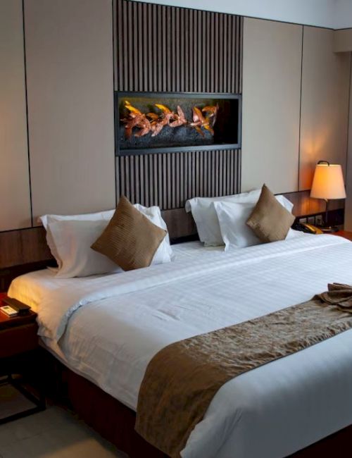 A neatly arranged hotel room with a large bed, decorative pillows, lamps, and a wall artwork, creating a cozy and inviting atmosphere.