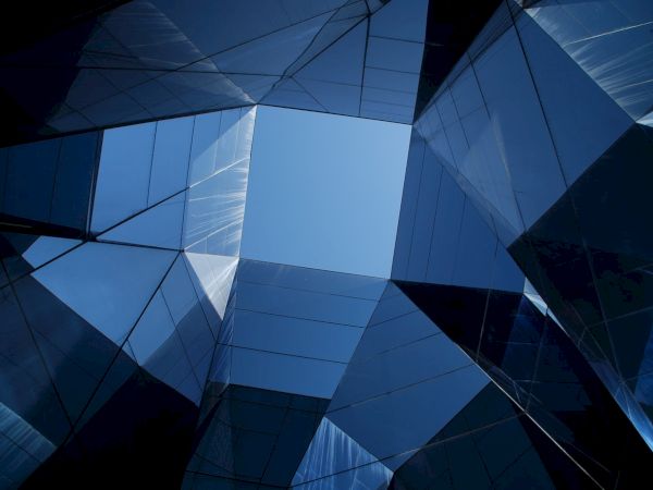 A geometric architectural pattern features reflective surfaces and sharp lines, creating an abstract view looking upwards toward the sky.