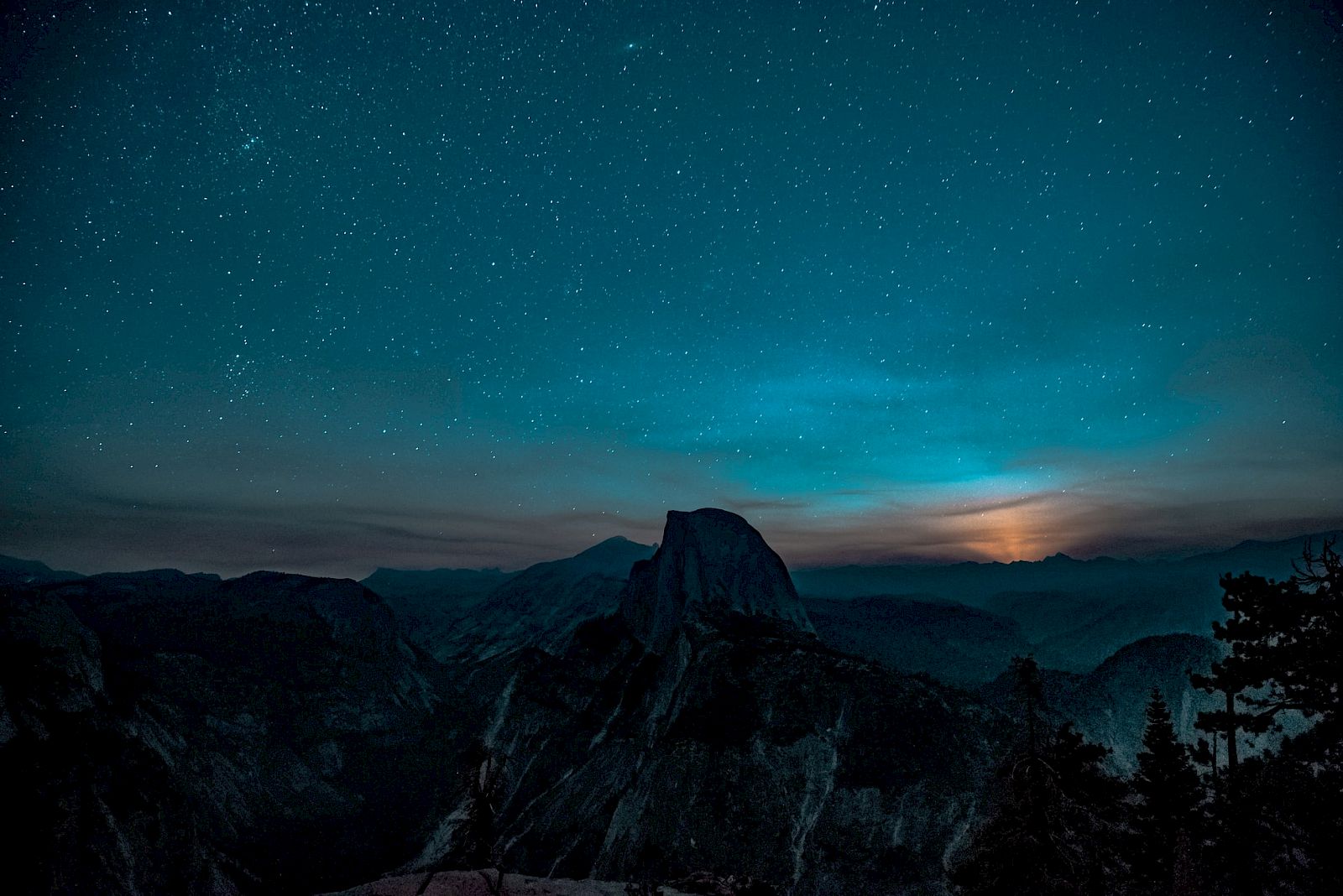 A breathtaking night sky filled with stars over a silhouette of mountains and trees, with a subtle glow on the horizon.
