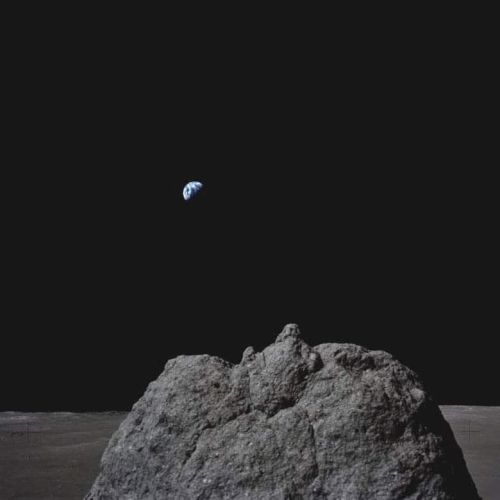 Rocky moon surface in the foreground with Earth visible in the distant black sky.