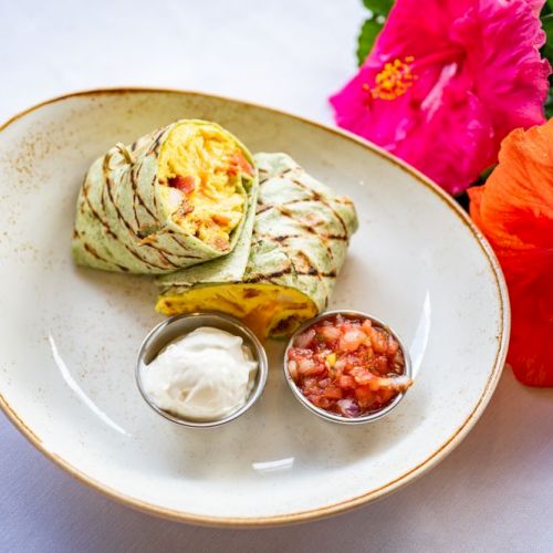A grilled wrap with a side of sour cream and salsa on a plate, accompanied by bright hibiscus flowers for decoration.