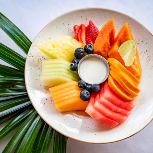 A plate with assorted fruits: strawberries, papaya, honeydew, mango, watermelon, blueberries, and a lime slice, surrounding a yogurt dip.