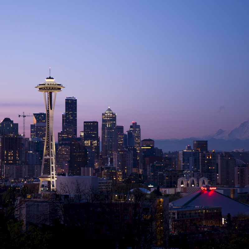 The image shows the Seattle skyline at dusk, featuring the Space Needle and Mount Rainier in the distance under a twilight sky.
