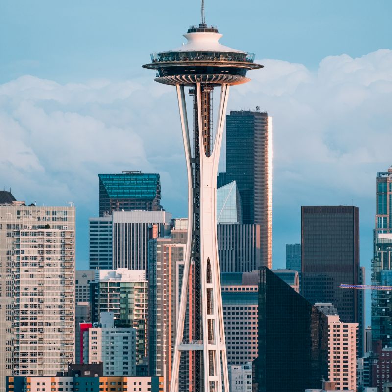 The image shows the Space Needle in Seattle with a backdrop of city skyscrapers under a cloudy sky.