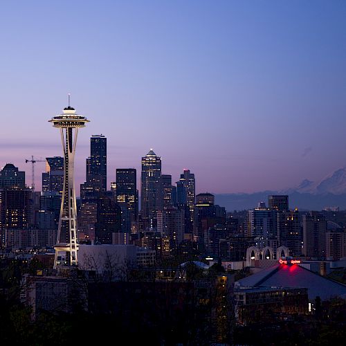The image shows the Seattle skyline at dusk, featuring the Space Needle and Mount Rainier in the background under a twilight sky.