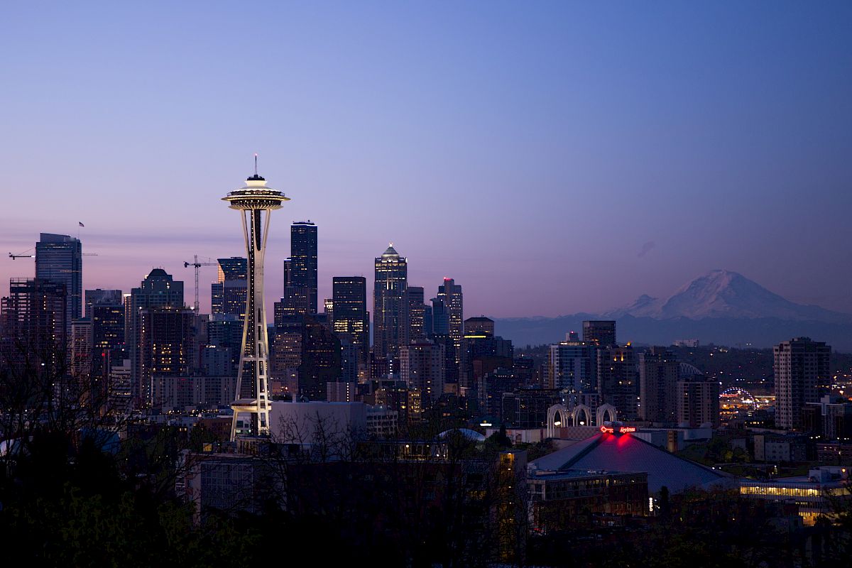 A twilight skyline featuring the Space Needle with a distant mountain silhouette under a purple sky.