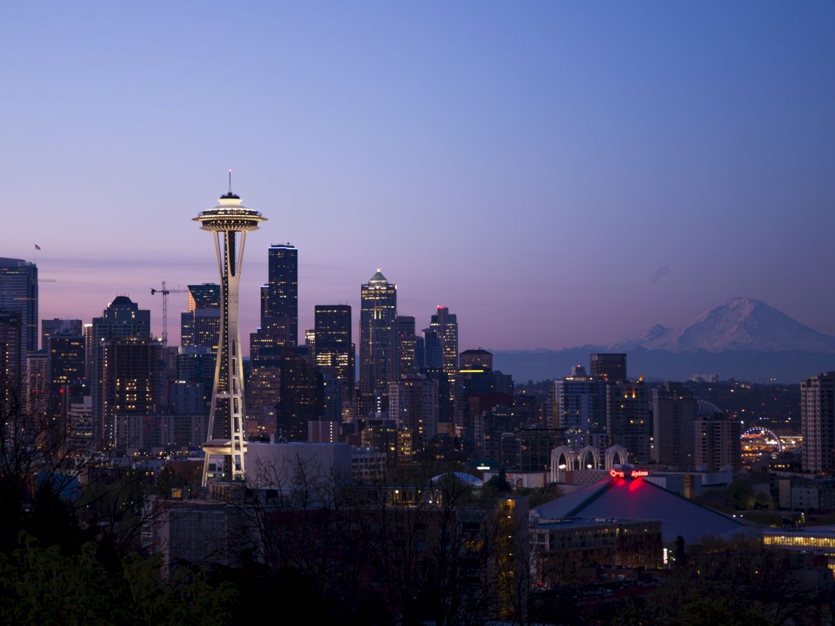 A twilight skyline featuring the Space Needle with a distant mountain silhouette under a purple sky.