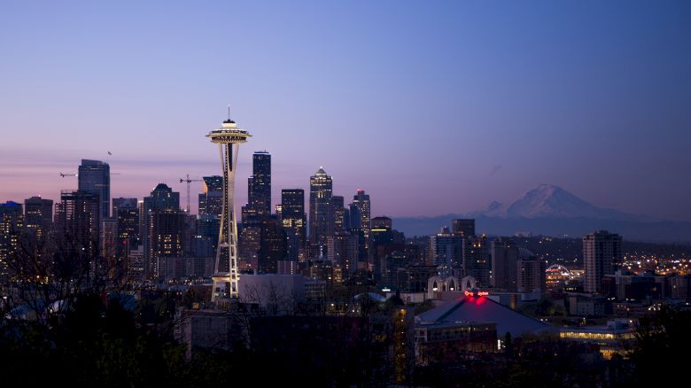 A twilight skyline featuring the Space Needle with a distant mountain silhouette under a purple sky.